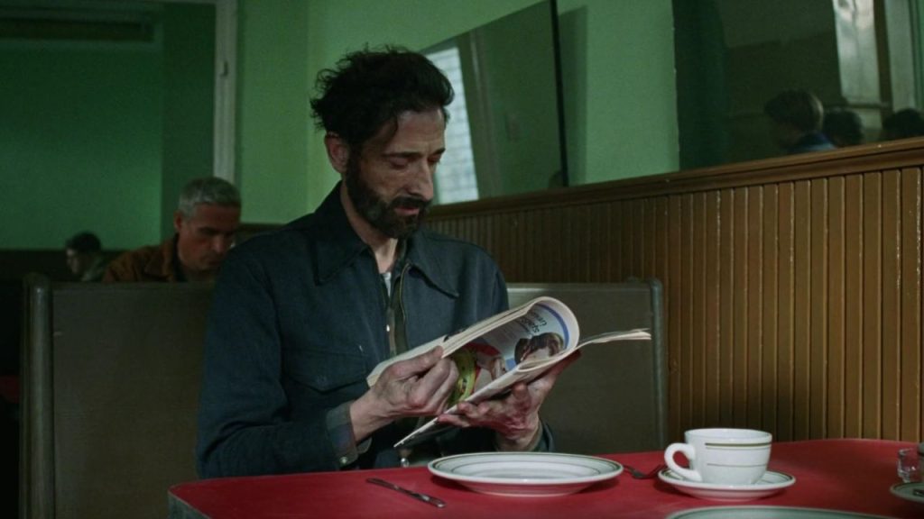 Adrien Brody reading a book in The Brutalist