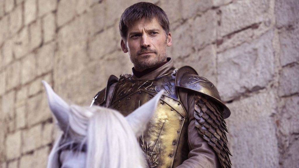 Jaime Lannister in his golden Kingsguard armor, mounted on a white horse against a stone wall background.