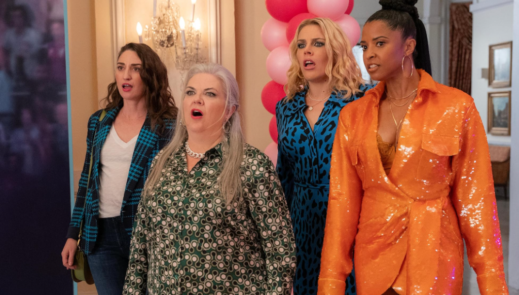 The main cast of Girls5eva posing together, featuring Busy Philipps, Renée Elise Goldsberry, Paula Pell, and Sara Bareilles, in a vibrant scene from the show.