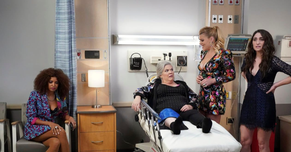 In a hospital scene from Girls5eva, with one lying on a hospital bed while the others stand beside her.