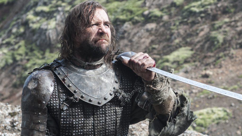 Sandor Clegane (The Hound) in battle-worn armor holding a bloodied sword. The image shows him outdoors in a mountainous landscape.