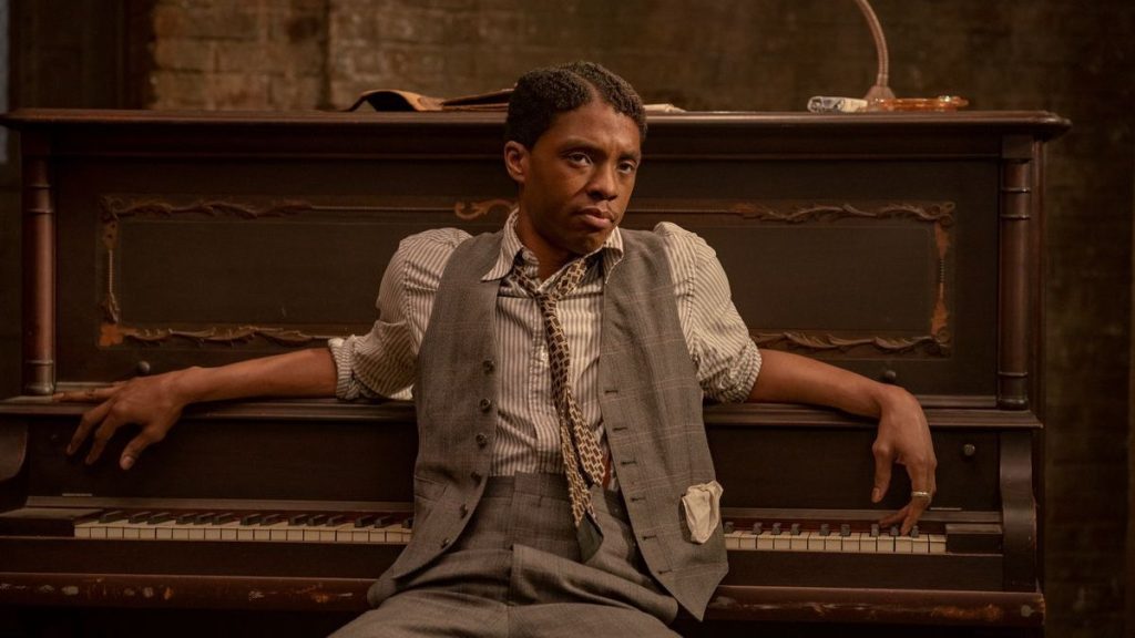 Chadwick Boseman as Levee in "Ma Rainey's Black Bottom," sitting at a piano in a vintage suit, with a contemplative expression.