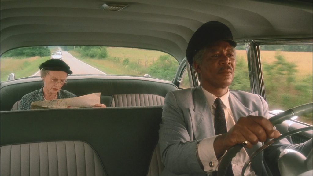 A scene from "Driving Miss Daisy" showing Daisy Werthan (Jessica Tandy) reading a map in the back seat while Hoke Colburn (Morgan Freeman) drives the car.