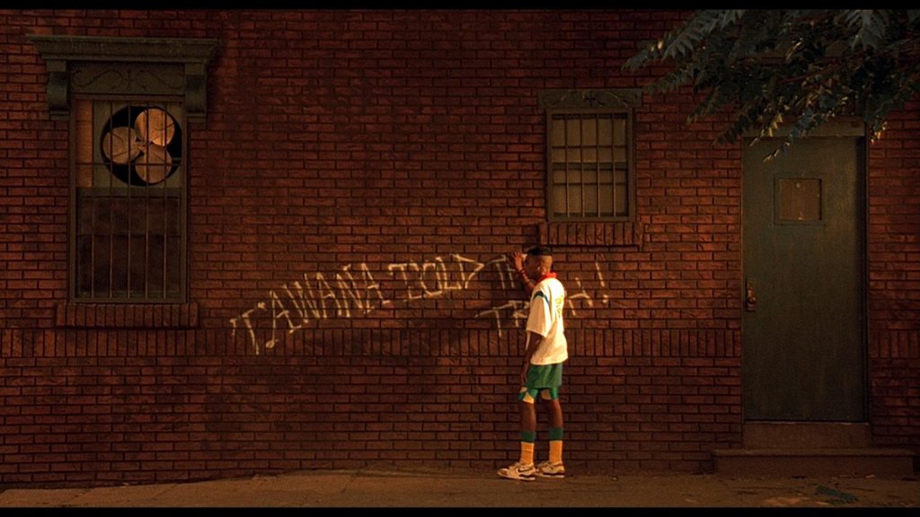 A scene from "Do The Right Thing" showing Mookie (Spike Lee) writing "TAWANA TOLD THE TRUTH" on a brick wall.