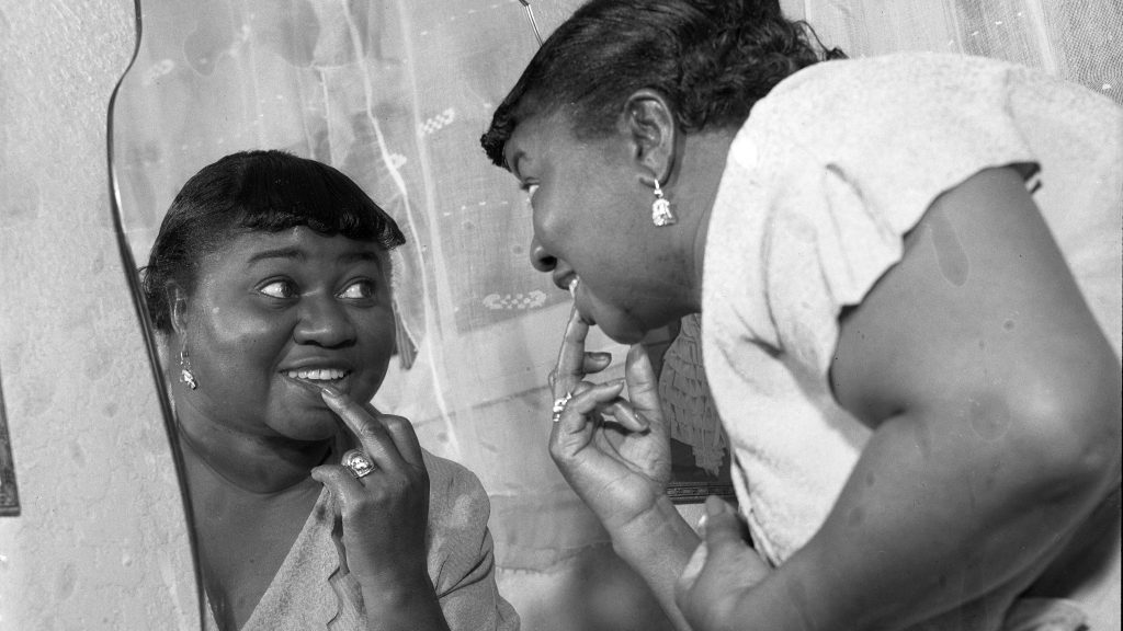 Hattie McDaniel looking at herself in a mirror, a historic black and white photograph of the first Black actor to win an Academy Award.