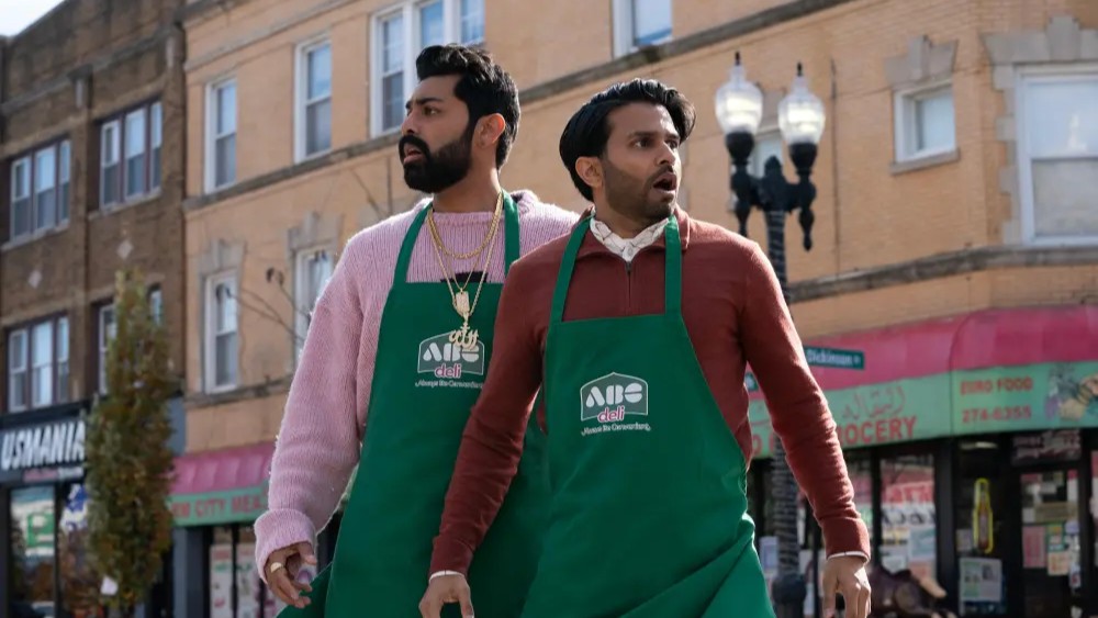 Asif Ali and Saagar Shaikh in green aprons over colorful shirts standing outside what appears to be a convenience store, from "Deli Boys."