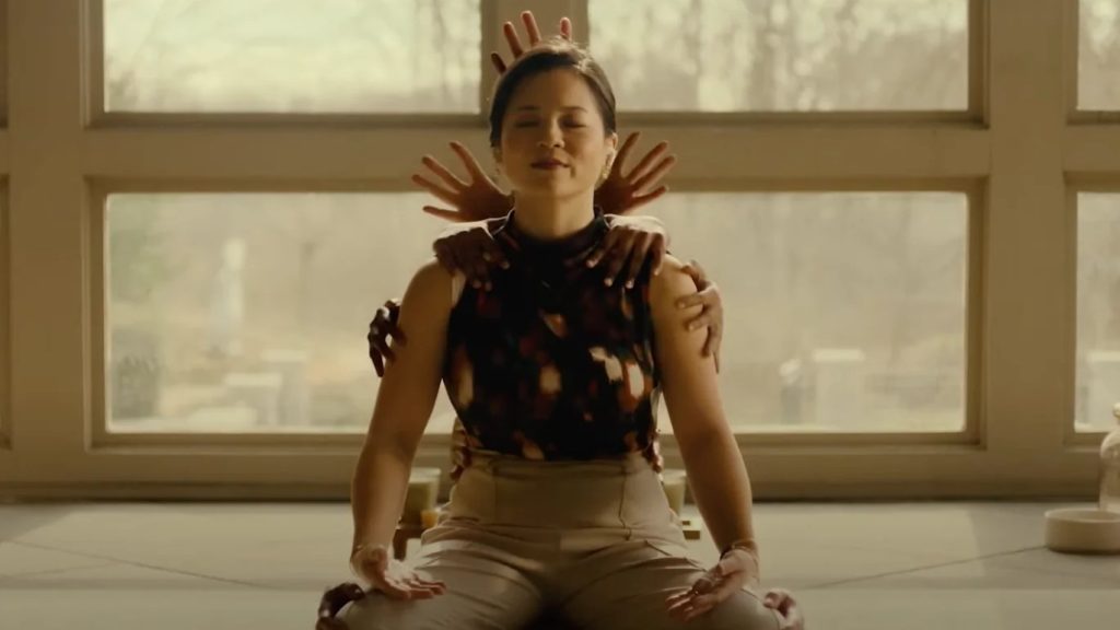 Kelly Marie Tran with her eyes closed sitting in meditation pose with hands visible behind her touching her shoulders, from "Control Freak."