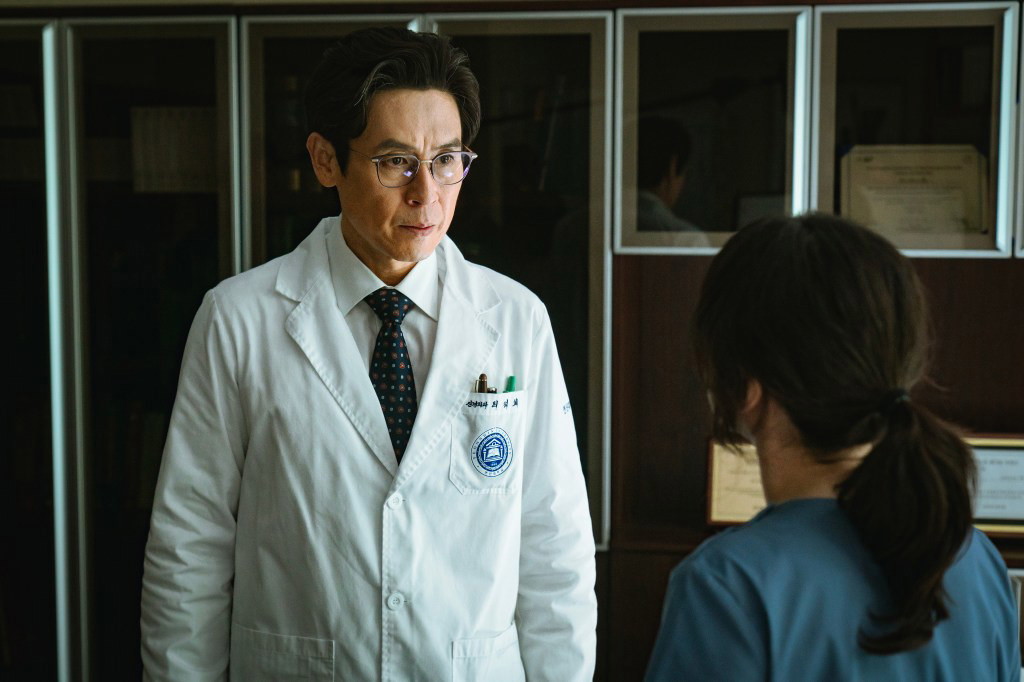 Sul Kyung-gu in a white doctor's coat and glasses looking serious, appearing to be speaking to Park Eun-bin (partially visible in the foreground), from the Korean medical thriller "Hyper Knife."