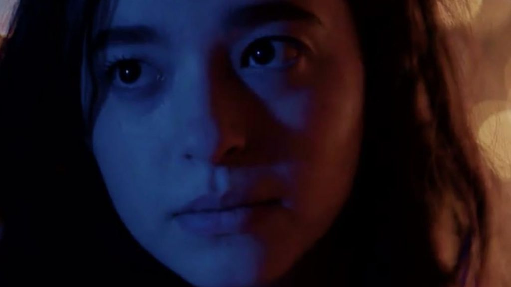 A close-up of Mikey Madison with blue-red lighting in a still from It Takes Three