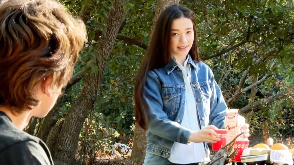 Mikey Madison preparing a table with food in the middle of the woods in a still from Liza, Liza, Skies Are Grey