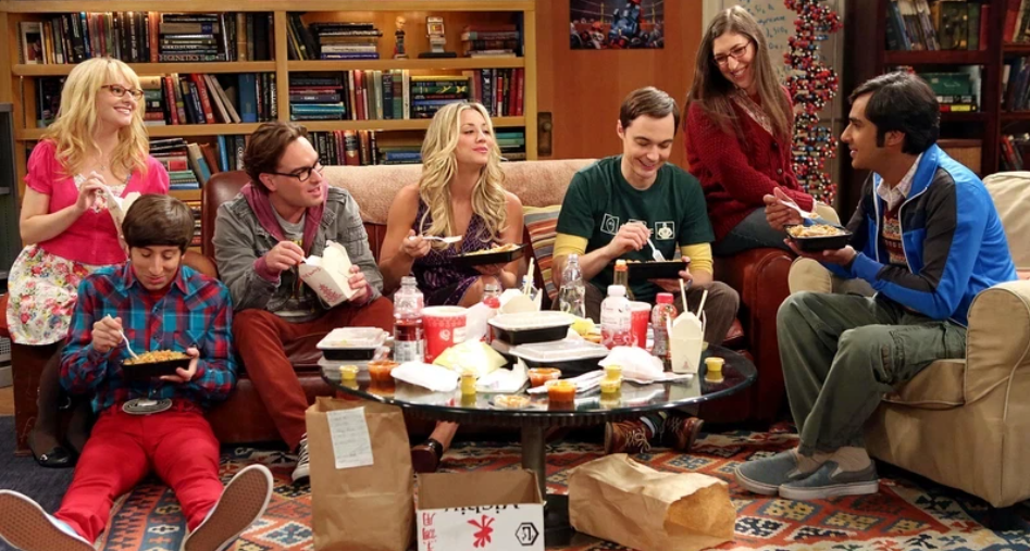 A scene from The Big Bang Theory featuring the main characters including Sheldon, Leonard, Penny, Howard, Raj, and Amy gathered together in a living room.