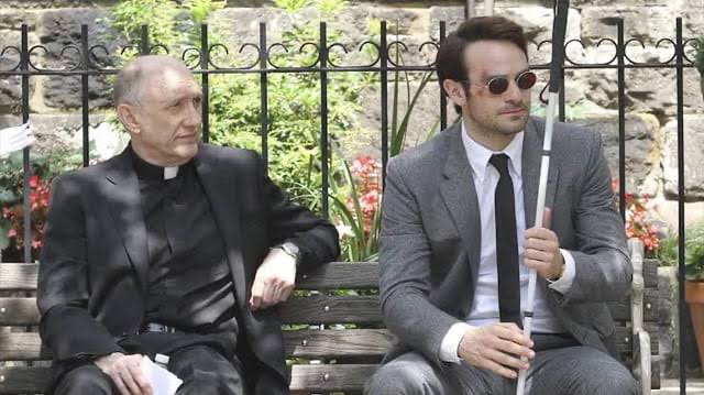 Charlie Cox’s Matt Murdock sitting with Father Paul Lantom in a still from Netflix’s Daredevil. 