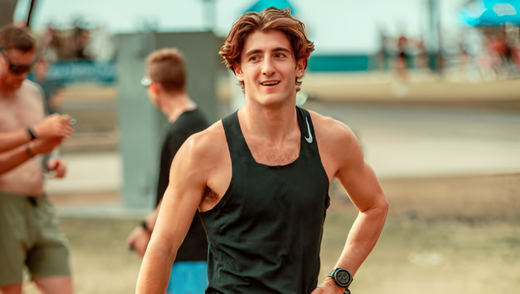 Jack Doohan wearing a black tank top and smiling, appears to be at a track or outdoor sporting facility.