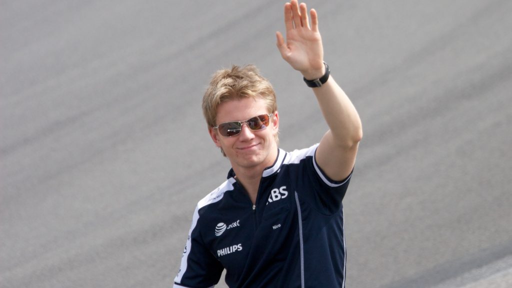 Nico Hülkenberg in Williams team casual wear from earlier in his career, waving to fans while wearing sunglasses.