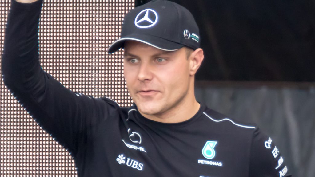 Valtteri Bottas in Mercedes team gear raising his arm to wave to fans at what appears to be a team event. He's wearing a black Mercedes cap and team shirt.