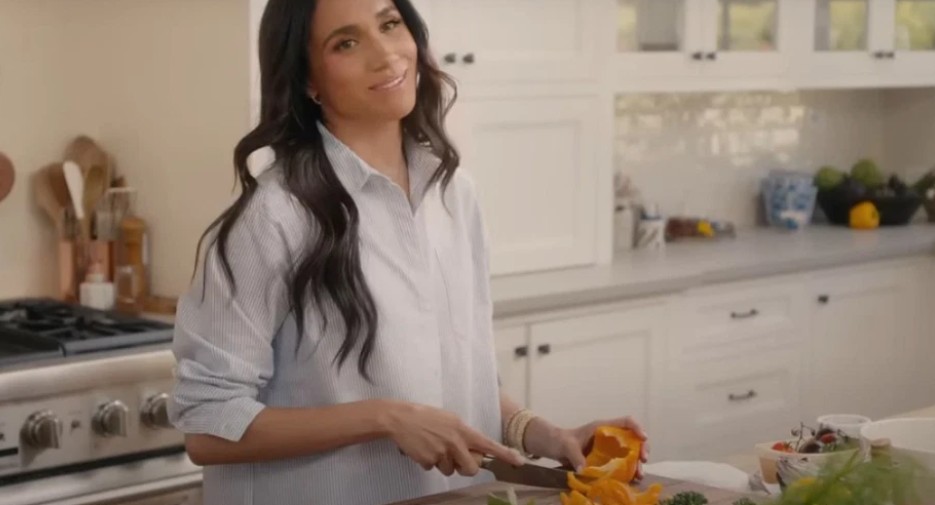 Meghan Markle posing in a white dress, standing gracefully in the kitchen.