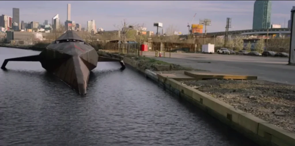 Dangerboat (voiced by Alan Tudyk) from The Tick, showing a sleek, black boat-like vehicle docked in water with a city skyline in the background.