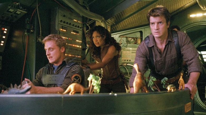 A scene from Firefly showing Alan Tudyk as Wash (left) at the pilot controls of the Serenity spaceship, with Gina Torres as Zoe and Nathan Fillion as Captain Malcolm Reynolds standing behind him.