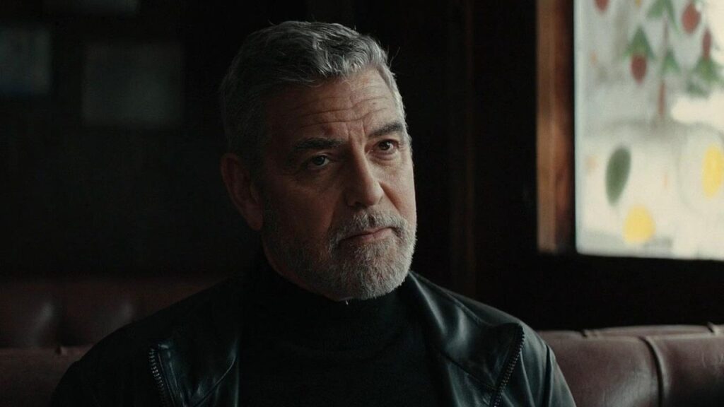 George Clooney looking at someone while sitting on a sofa in Wolfs