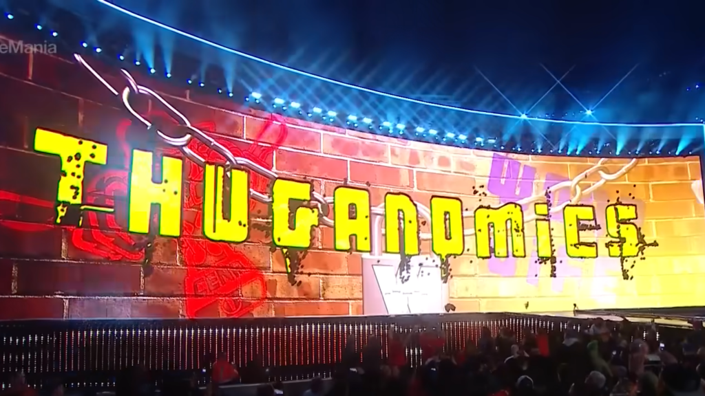 A large "THUGANOMICS" text display on a WrestleMania stage set, representing John Cena's early "Doctor of Thuganomics" character. The text is in yellow graffiti-style font against a brick wall backdrop with colorful lighting.