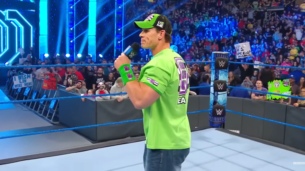 23 Years of John Cena: Every Year in WWE, Ranked 6 John Cena in a bright green t-shirt and cap, standing in a WWE ring with a microphone. The crowd can be seen in the background.