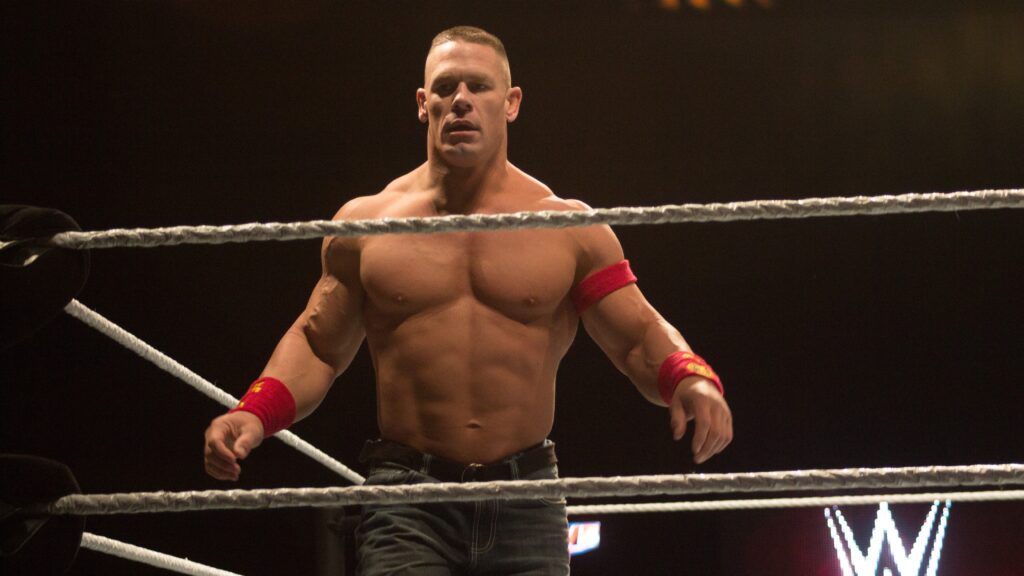 John Cena in jean shorts and red wristbands looking intense while standing in a WWE ring.