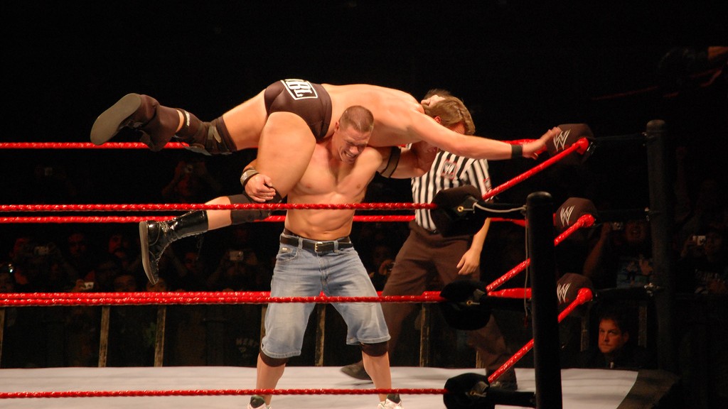 John Cena performing his signature Attitude Adjustment move, lifting Bradshow across his shoulders in a WWE ring.