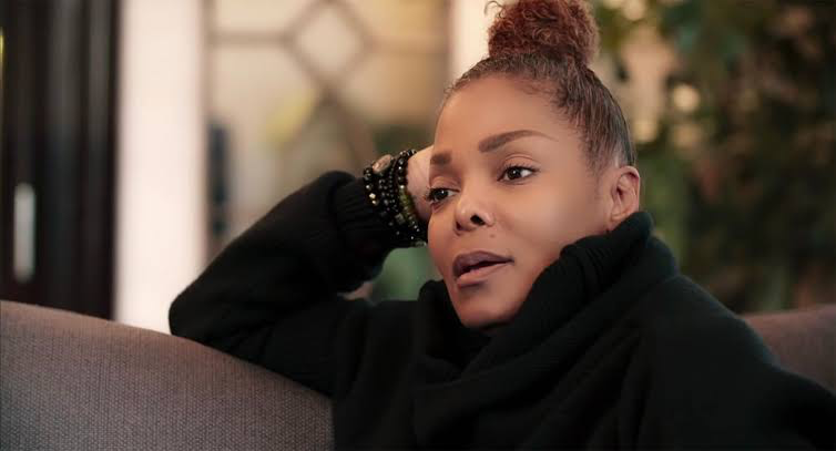 Janet Jackson sitting on a couch while talking.