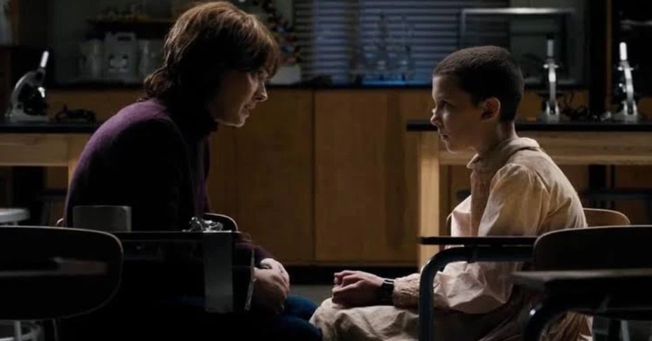 Winona Ryder and Millie Bobby Brown sitting across from each other, sharing a quiet moment in a scene from Stranger Things.