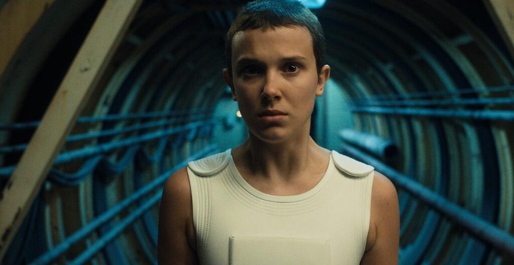 Millie Bobby Brown as Eleven in a serious moment from Stranger Things, displaying a determined and focused expression. 