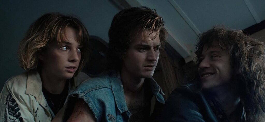 Maya Hawke, Joseph Quinn, and Joe Keery in a tense and scary scene from Stranger Things, looking terrified as they face a looming threat.