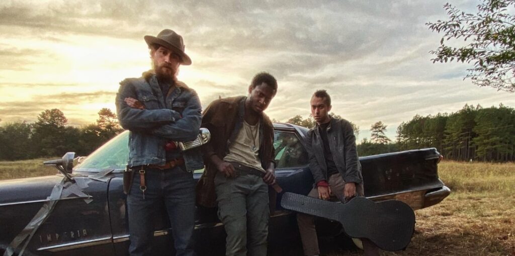 Brendan Bradley, Nican Robinson, and Jordon Bolden striking a pose by the car in a scene.