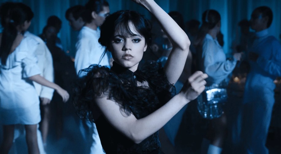 Jenna Ortega as Wednesday Addams, is wearing a black dress, and confidently dancing. 