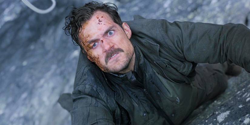 Henry Cavill as August Walker hanging off a cliff with a portion of his face burnt off.