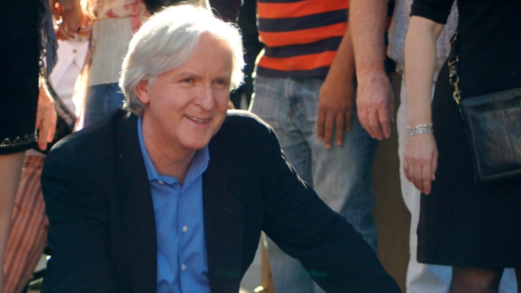 10 Most Successful Non-American Directors in Hollywood 6 James Cameron wearing a dark blazer over a blue shirt, smiling at a ceremony to receive a star on the Hollywood Walk of Fame. He's photographed from a slight angle with people visible in the background.