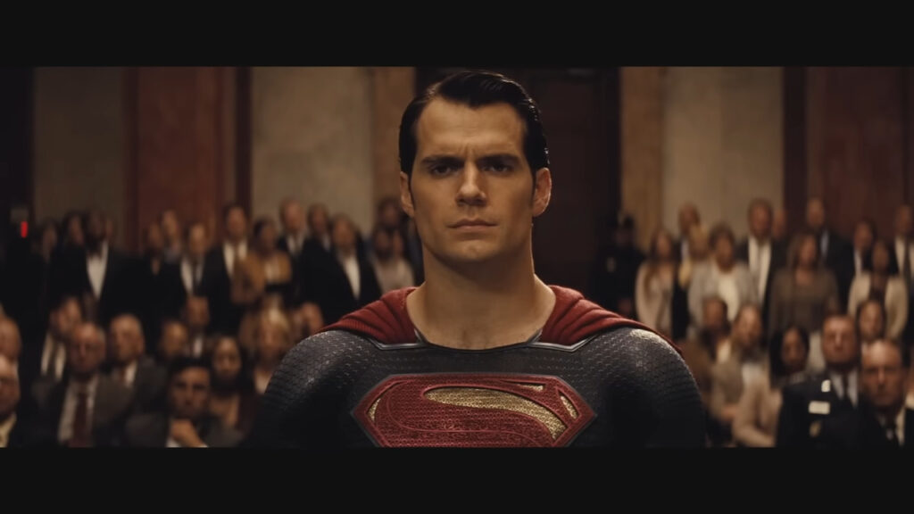 Henry Cavill in the Superman suit inside the courtroom surrounded by people 