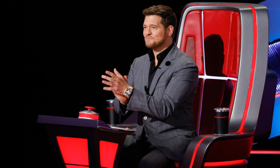 Michael Bublé clapping while sitting in the red judge's chair in the reality show The Voice.