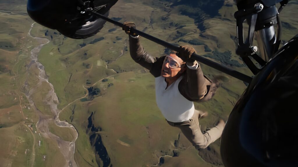 Tom Cruise hanging on the axle of a plane's wheel while in air in a still from Mission: Impossible - The Final Reckoning 