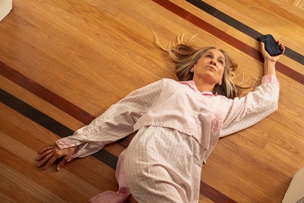 Carrie is lying down on the floor with her cellphone in one hand.