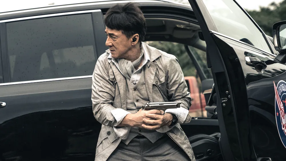 The Shadow's Edge Looks Like Police Story 4 But Jackie Chan Is Not Trying to Make You Laugh in His Next Movie 1 Jackie Chan behind a car with his gun drawn out in a still from Vanguard.