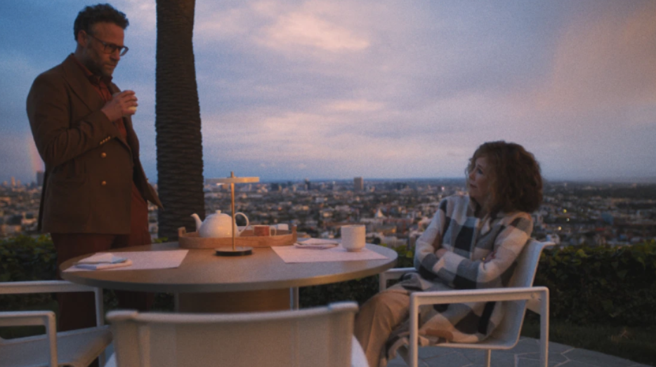 20 Absolutely Best TV Shows to Watch Right Now (June 2025) 2 Patty is sitting on a deck chair. Matt is standing on the other side of the table. Both are looking at each other.