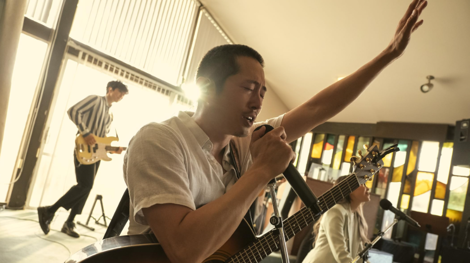 20 Absolutely Best TV Shows to Watch Right Now (June 2025) 48 Danny is singing his heart out. A guitar is hanging from his neck. He is holding the microphone with one hand, and his other hand is up in the air.