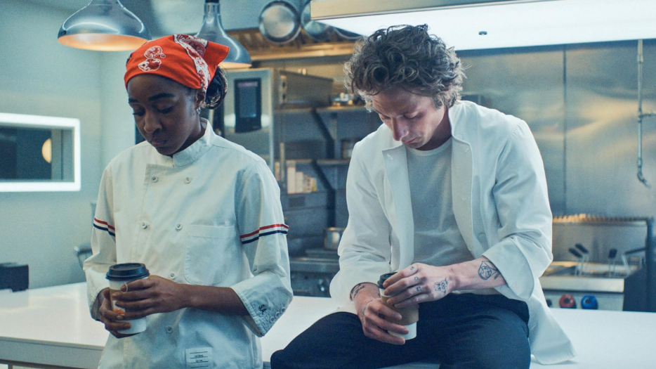 20 Absolutely Best TV Shows to Watch Right Now (June 2025) 38 Sydney is standing while Carmen is sitting on the table beside her. Both are looking down at their coffee cups.