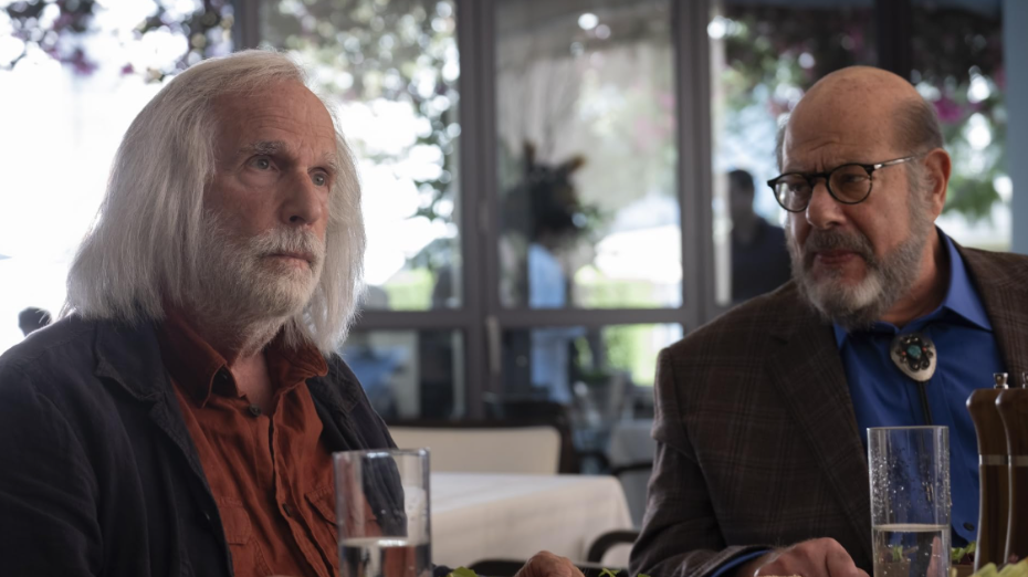 20 Absolutely Best TV Shows to Watch Right Now (June 2025) 44 Gene and Tom are sitting in a restaurant. Gene is looking ahead at someone while Tom stares at Gene. Gene has long white hair and a white beard.