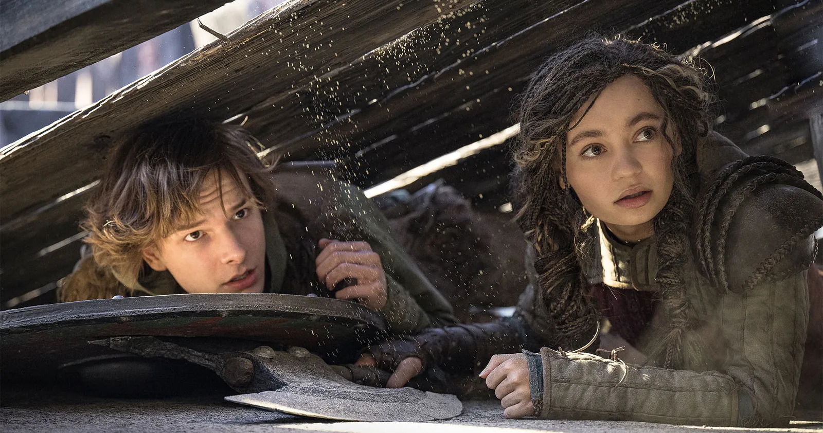 A still from How To Train Your Dragon (2025) featuring Hiccup and Astrid hiding under cover in the arena