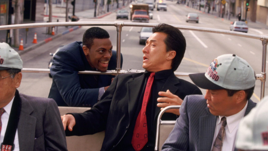 Carter is hanging from the back of a double-decker bus. Lee is sitting at the rear of the bus, turning to look at Carter.
