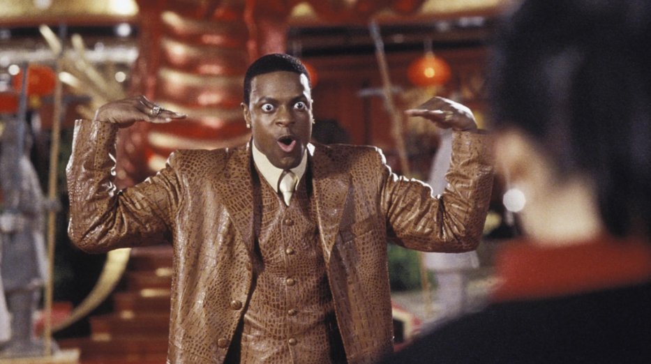 Carter is wearing a shiny brown suit, making a funny face, and lifting his hands dramatically.