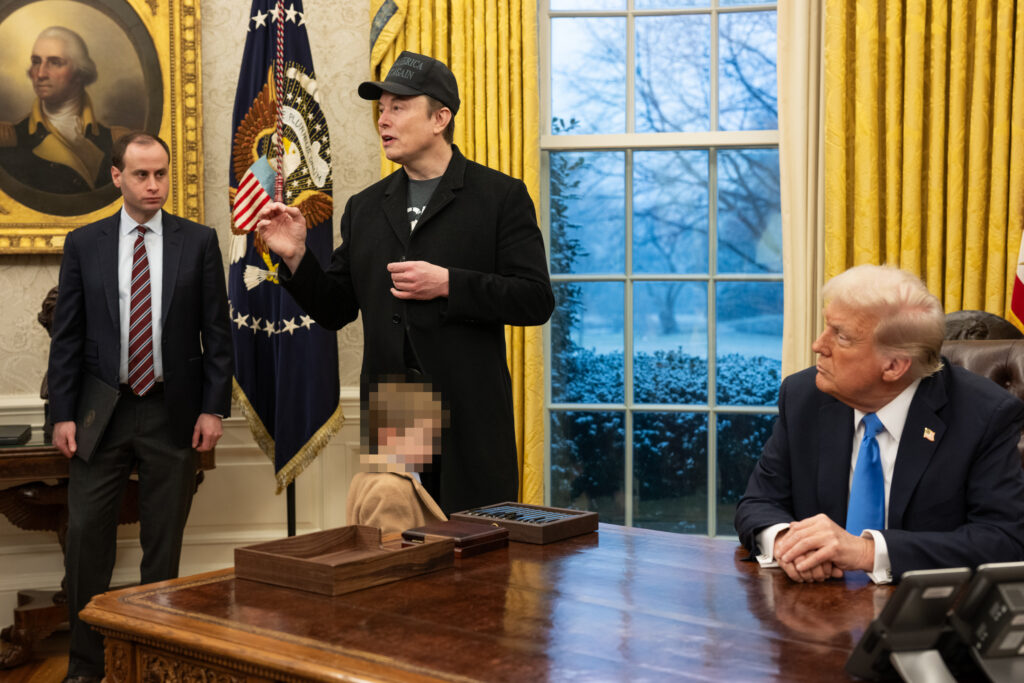 Elon Musk explaining something while Donald Trump sits.