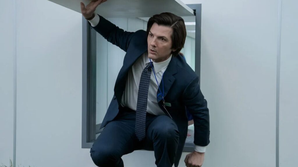 20 Absolutely Best TV Shows to Watch Right Now (June 2025) 55 Mark in a dark business suit with a patterned tie crouches in a modern white corridor, with one hand raised up to hold the trap-door he came through.