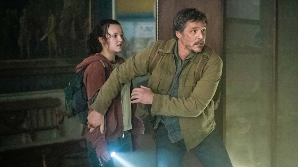 20 Absolutely Best TV Shows to Watch Right Now (June 2025) 60 Joel in olive-colored clothing protectively holds Ellie in reddish garments as they navigate a dark indoor space, with Ellie holding a flashlight.
